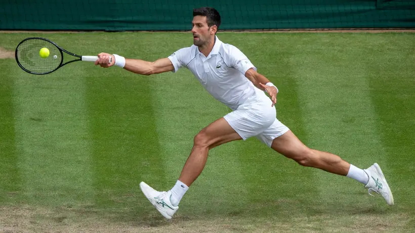 Novak Djokovic, tout vêtu de blanc, retour coup droit en bout de ligne sur le gazon de Wimbledon.
