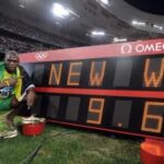 Usain Bolt, accroupi, avec le drapeau de la Jamaïque, devant le chronomètre qui affiche la mention "New WR" et son temps sur 100 mètres "9.69"